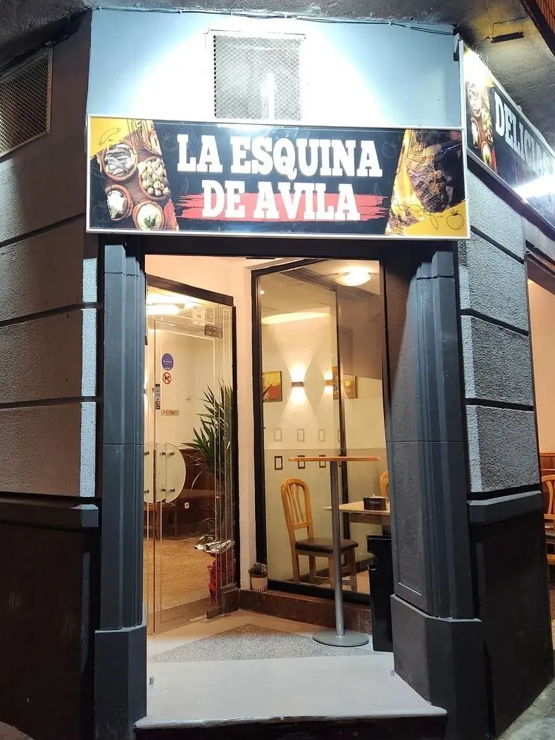 Puerta de cristal y rótulo La Esquina de Ávila en la fachada, de noche