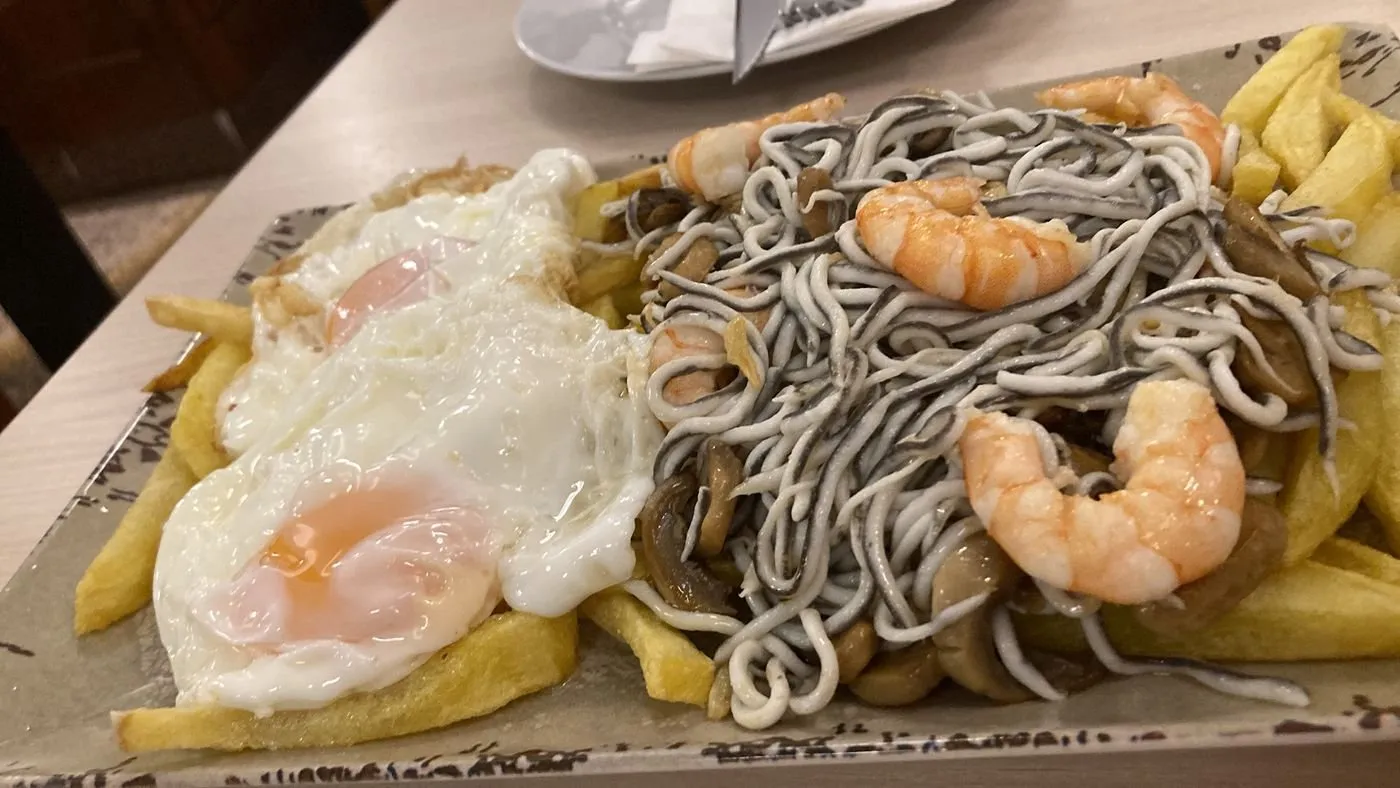 Huevos fritos con patatas, gulas, gambas y champiñones en una fuente