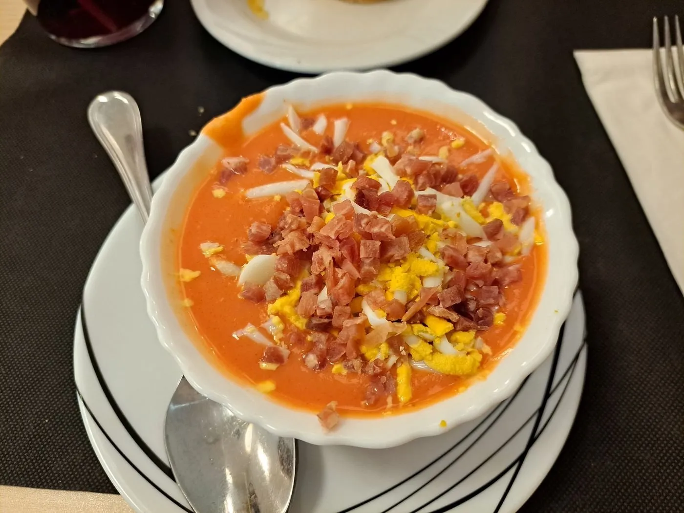 Salmorejo con taquitos de jamón y huevo duro picado en un cuenco blanco
